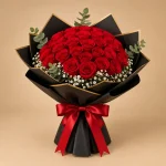 50 red roses arranged in a full dome with baby's breath and eucalyptus in black and gold wrapping