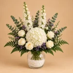 Tall white flower arrangement with cream roses, snapdragons, purple statice and three focal flower options in a ribbed glass vase