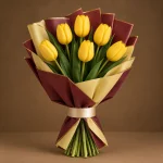 Six golden yellow tulips with fresh green foliage in maroon and warm-gold wrapping